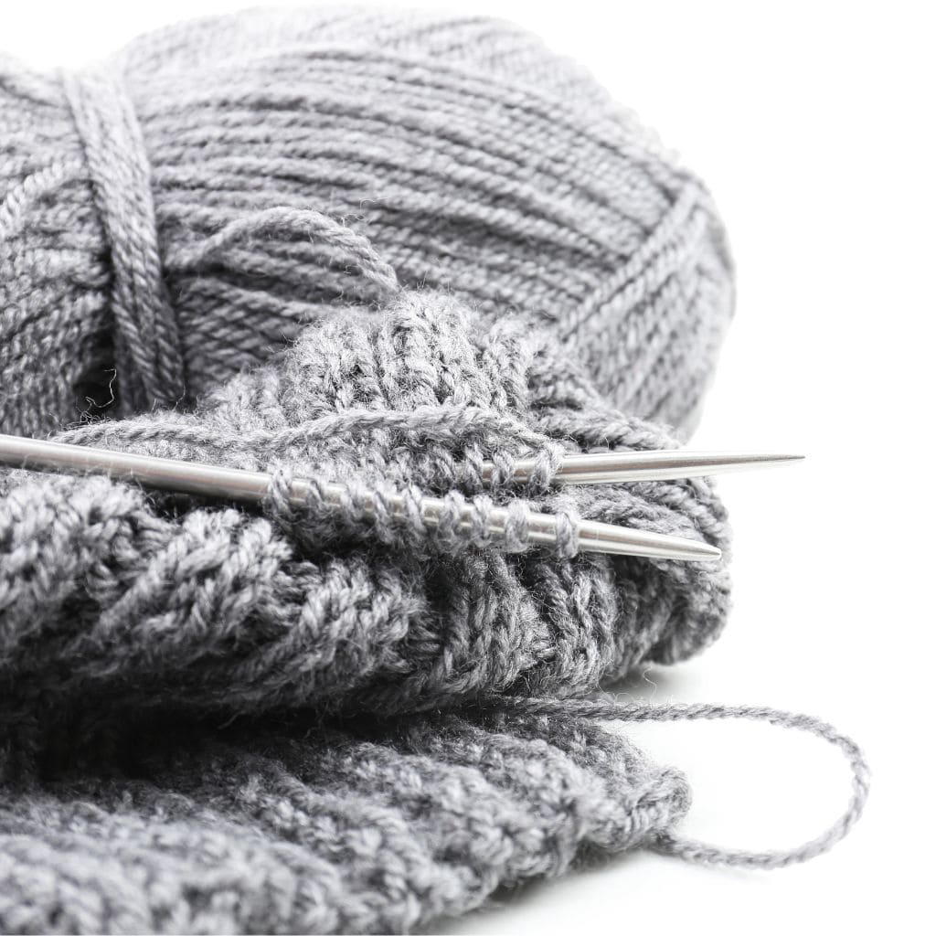 A gray skein of yarn and knitting needles with a partially knit project