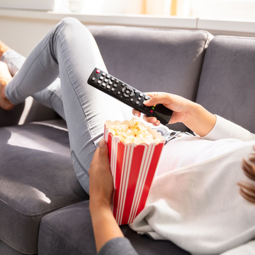 Woman on couch with TV remote and bucket of popcorn
