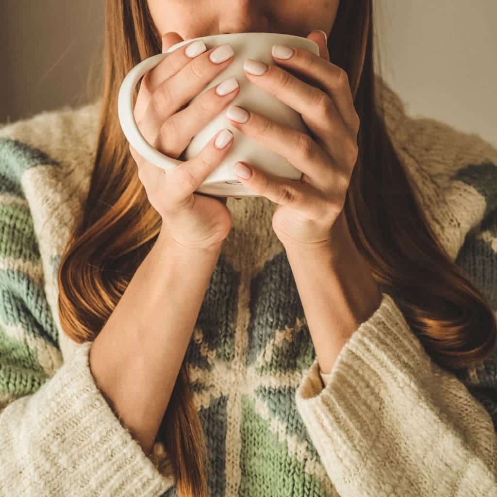 A woman with her hands wrapped around a warm mug of tea