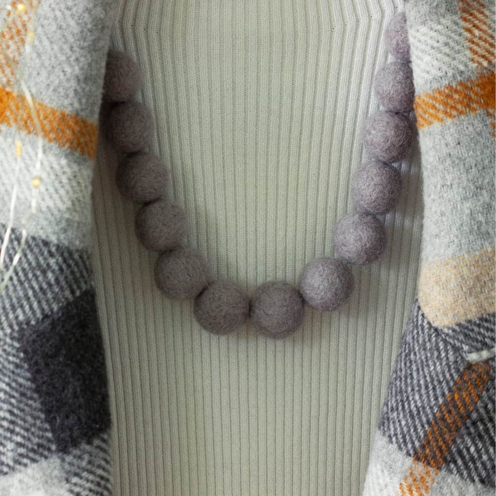 A necklace made of large, grey felted wool beads worn over a white ribbed top and a grey and orange plaid jacket.