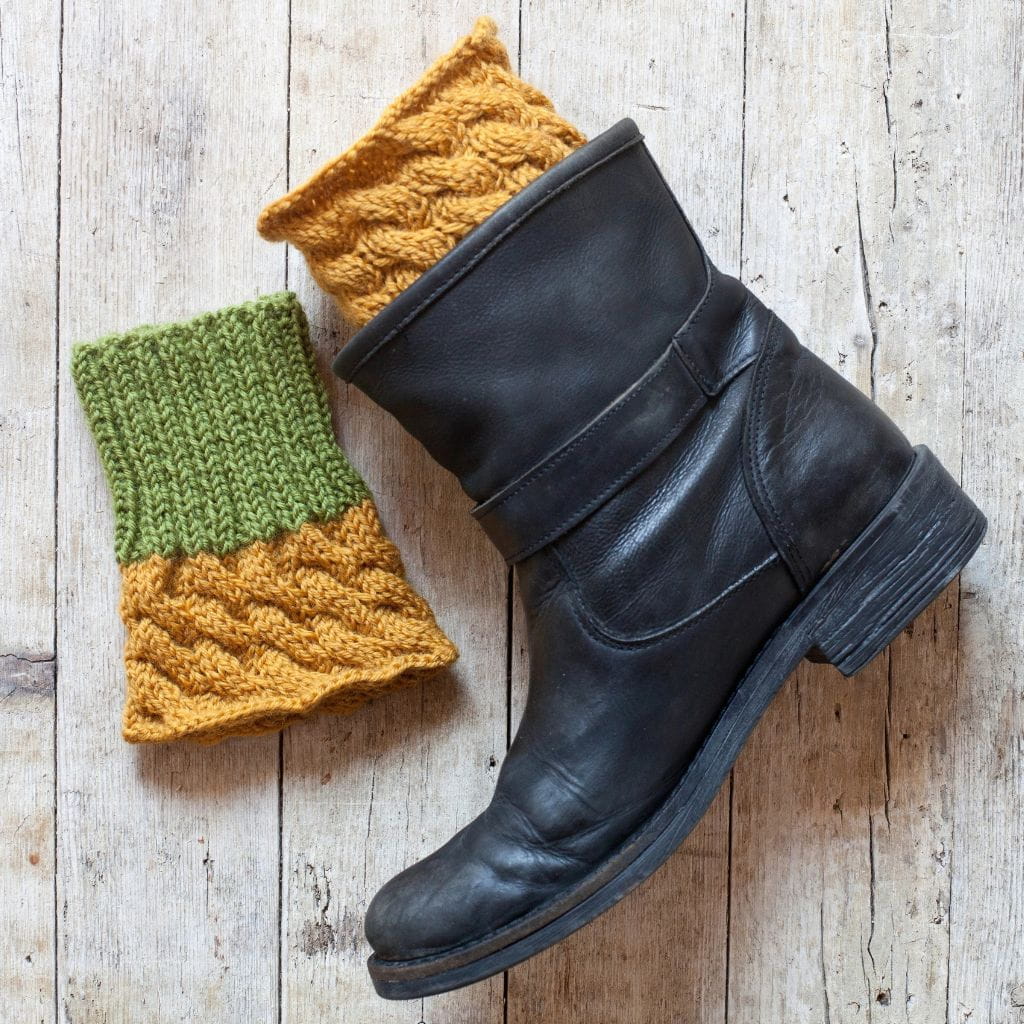 A black leather boot and two knit boot cuffs with yellow cable-knit details and green ribbed trim.