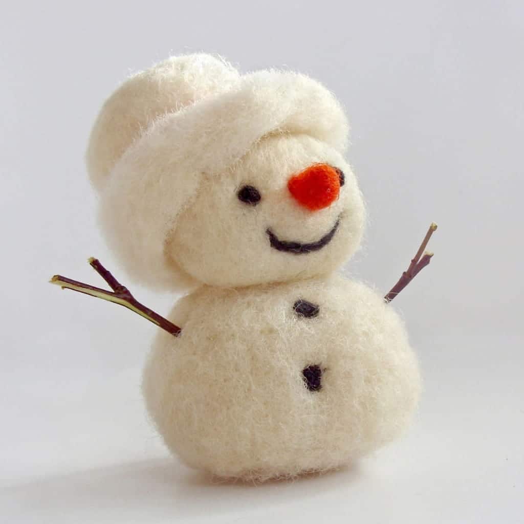A small, handmade felt snowman with a carrot-colored nose, stick arms, and a matching hat.