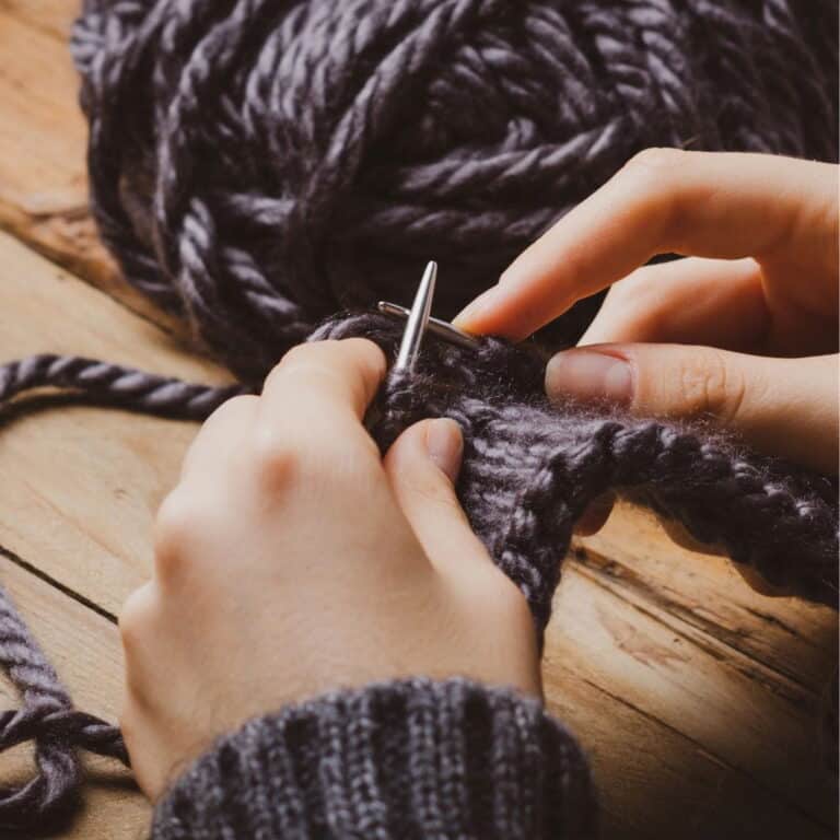 Close-up of hands knitting with dark grey yarn using silver needles.